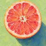 Doorgesneden roze grapefruit van bovenaf op een lichtgroene achtergrond met een blauwe schaduw.