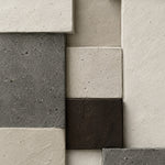 Relief of staggered blocks in cream plaster, dark grey concrete and one dark brown block