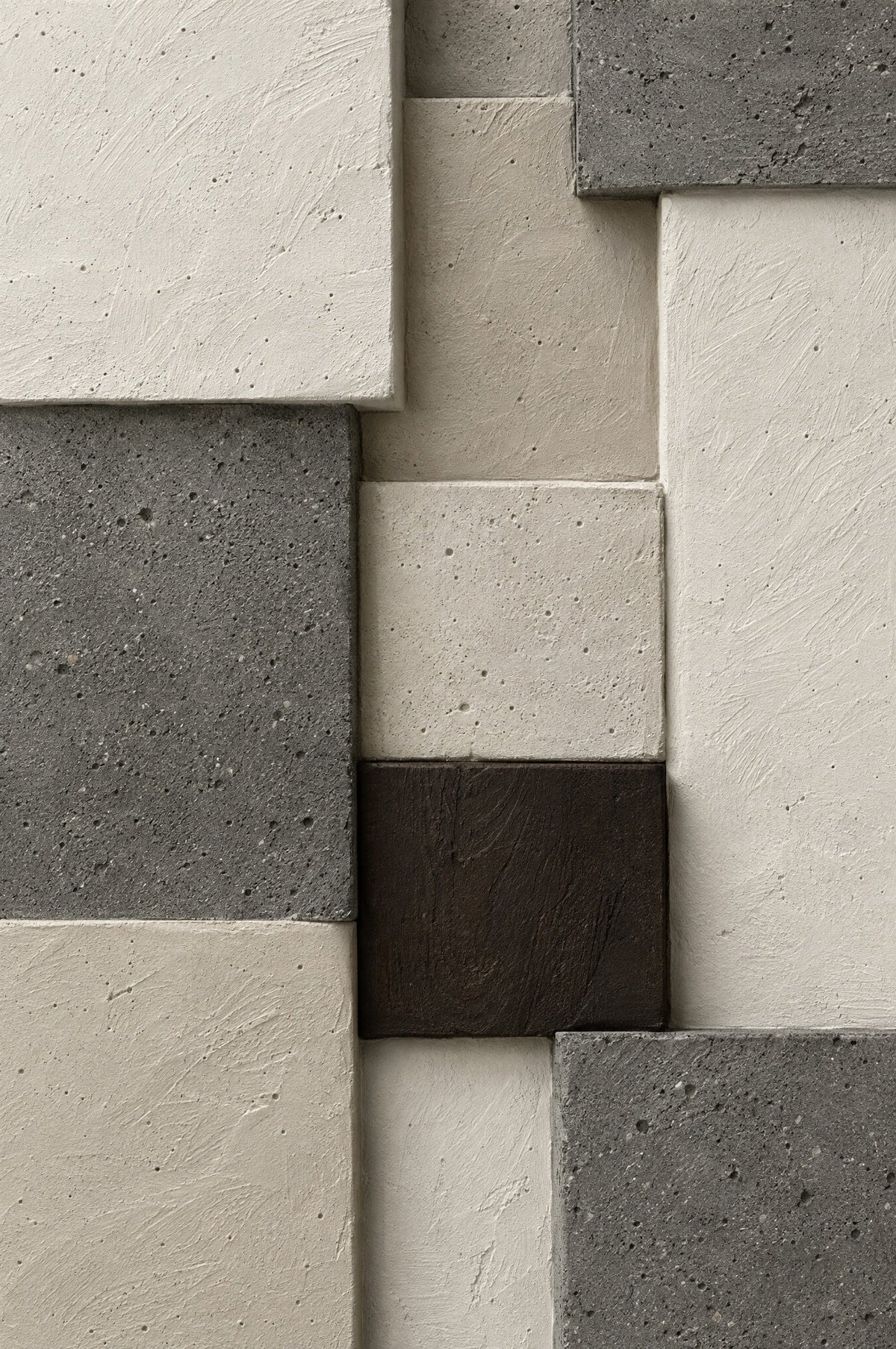 Relief of staggered blocks in cream plaster, dark grey concrete and one dark brown block