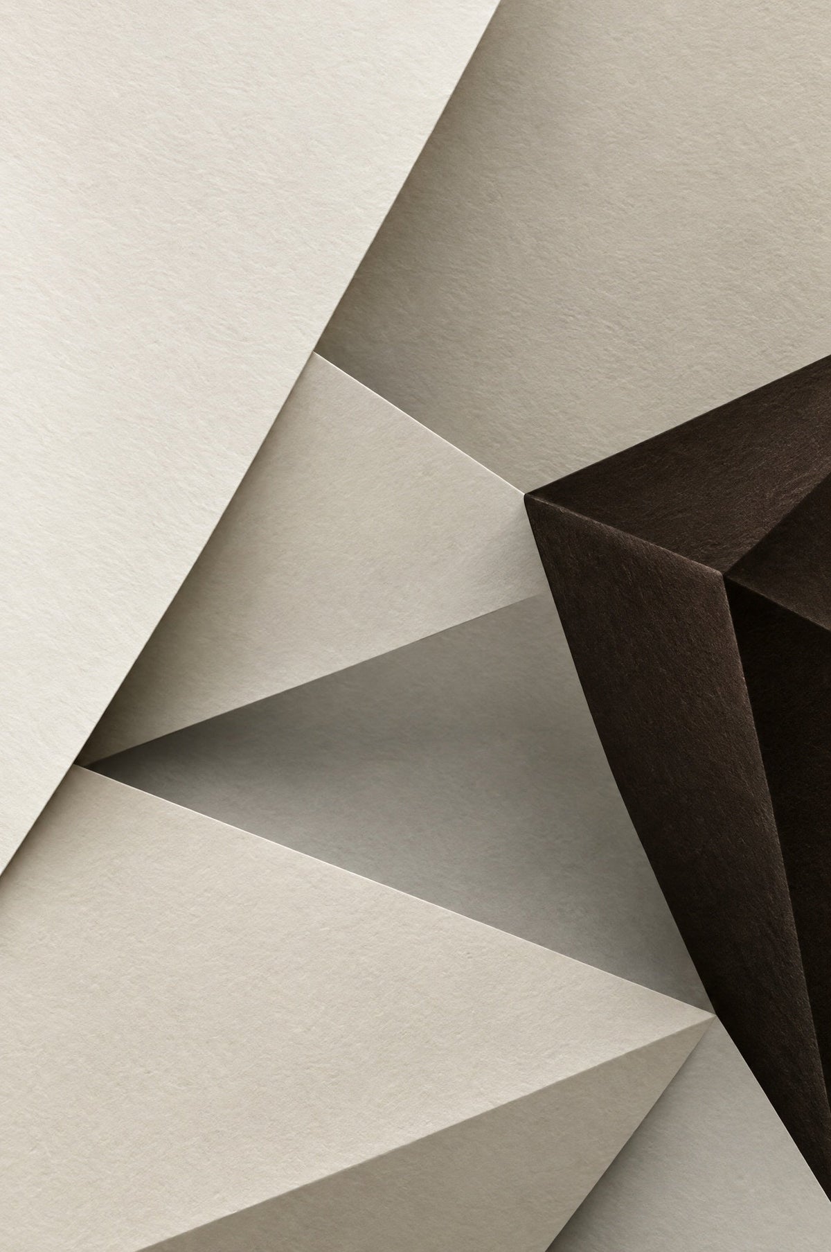 Gefaltetes elfenbeinfarbenes Papier mit schrägen Flächen und einer dunkelbraunen facettierten Form