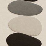 Vertical stack of pebbles in black, mineral grey and bone on an off-white ground